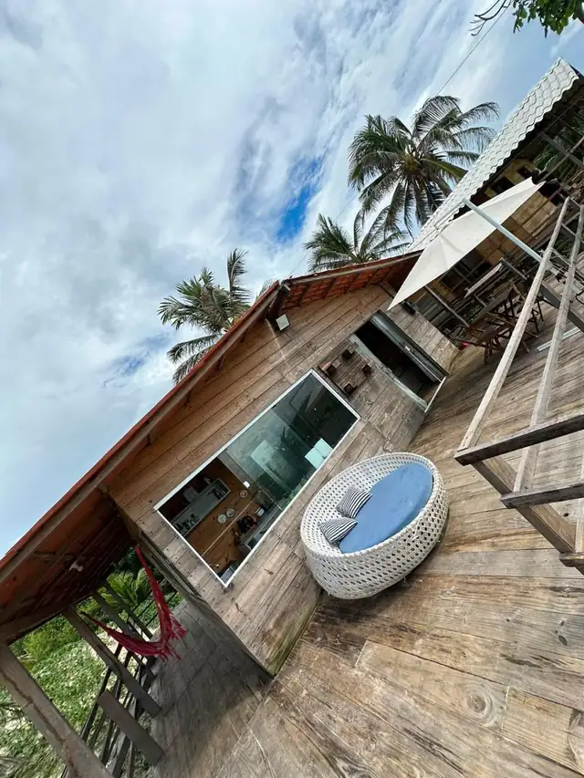 Deck do Pé na Areia, com o sofá redondo, a janela de vidro e os coqueiros
